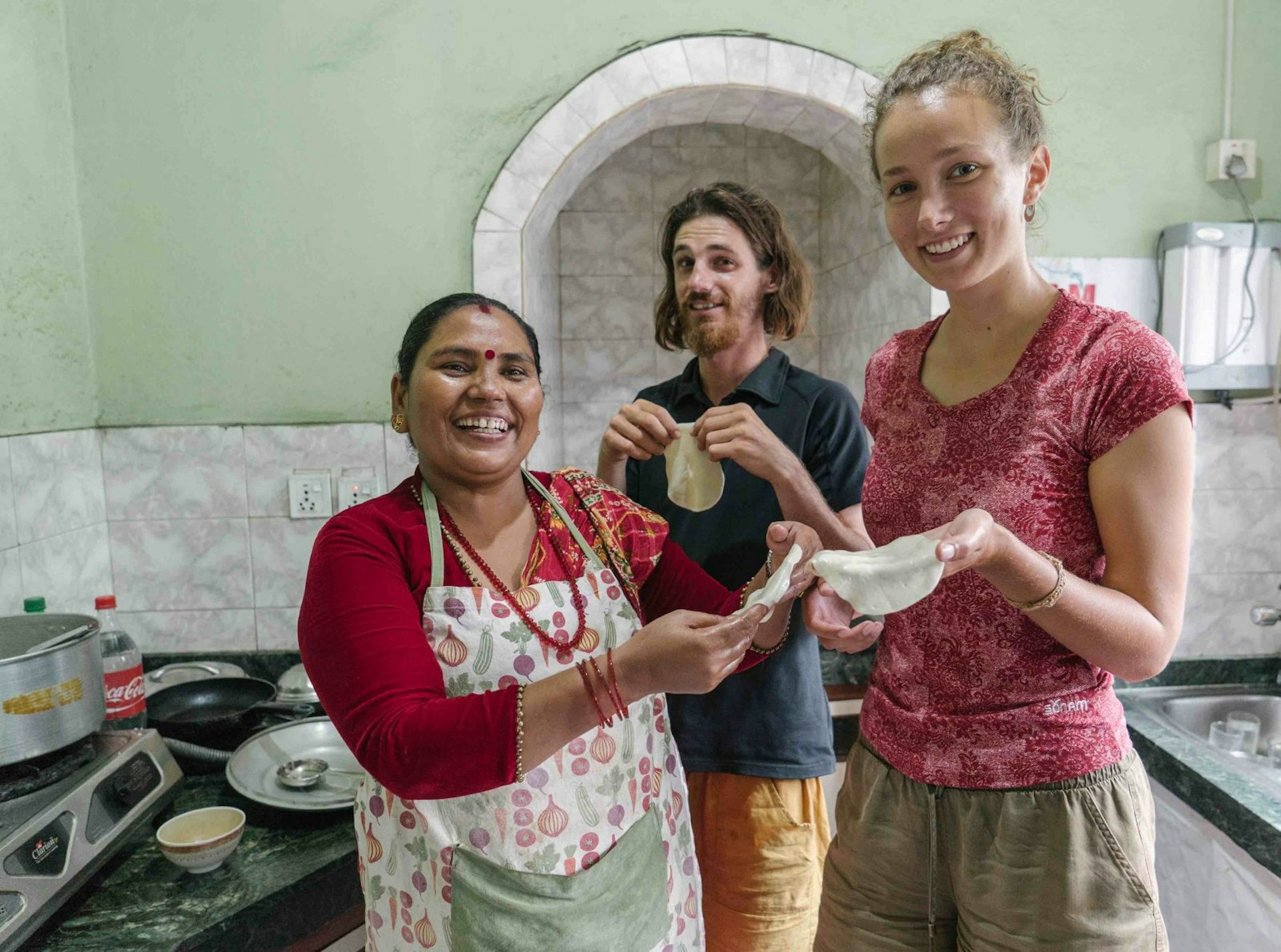 A male and female traveller hold chapatis while posing with a woman leading a cooking course