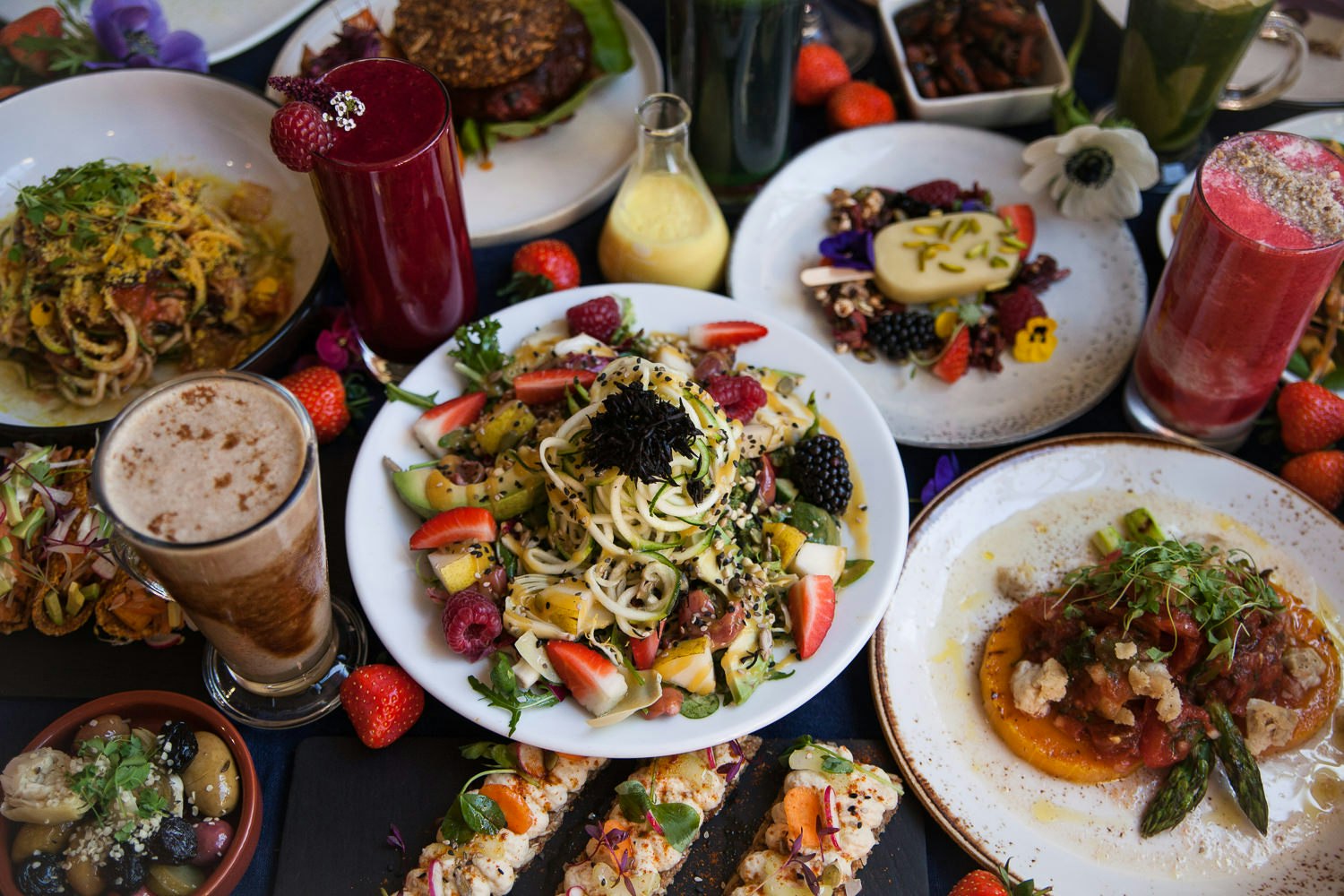 A huge colourful spread of food arranged on a table at the Wild Food Cafe, full of vegetables, fruit, noodles, juices and smoothies.