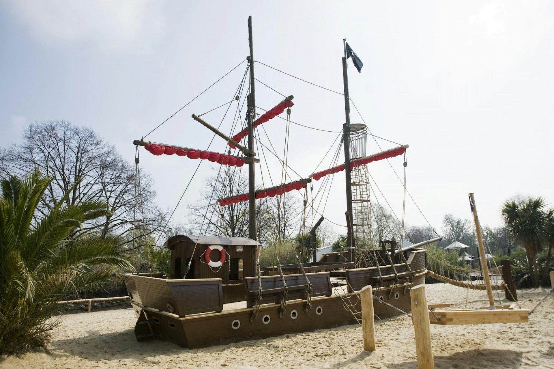 A climbing frame shaped like a pirate ship sits in a massive sandpit in Princess Diana Memorial Playground