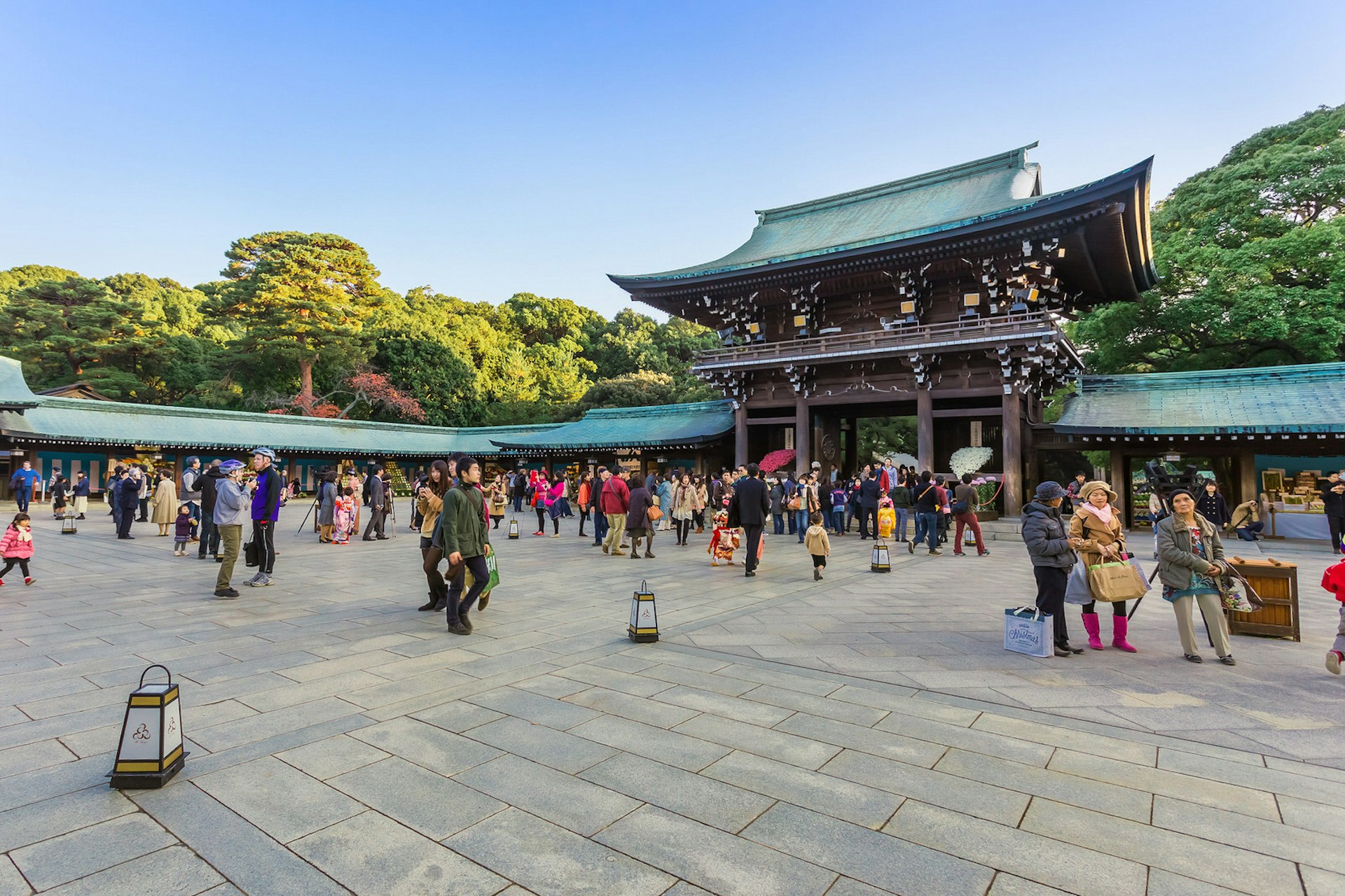Meiji-jingū - a large wooden shrine in Tokyo with a sloping green roof. A crowd of people gather in the shrine's courtyard, with trees visible beyond the shrine's walls.
