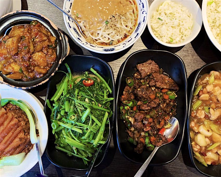 A selection of Sichuan and Hunan dishes at Yipin restaurant. The close-up shot shows a chicken dish, a beef dish, green vegetables and chillies, rice, noodles and seafood in black and white bowls.