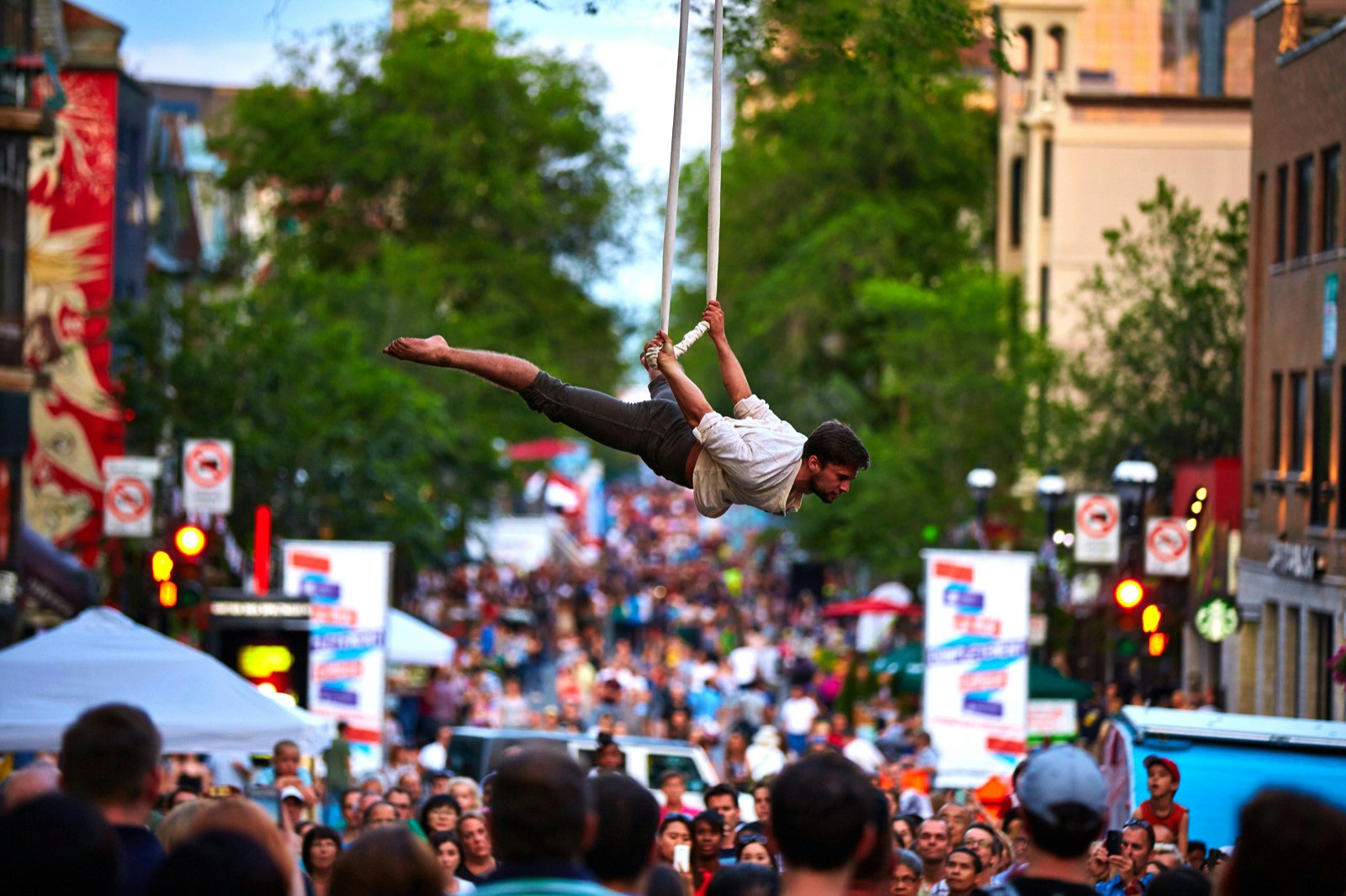A circus acrobat is suspended above a crowd of spectators in the streets of Montreal