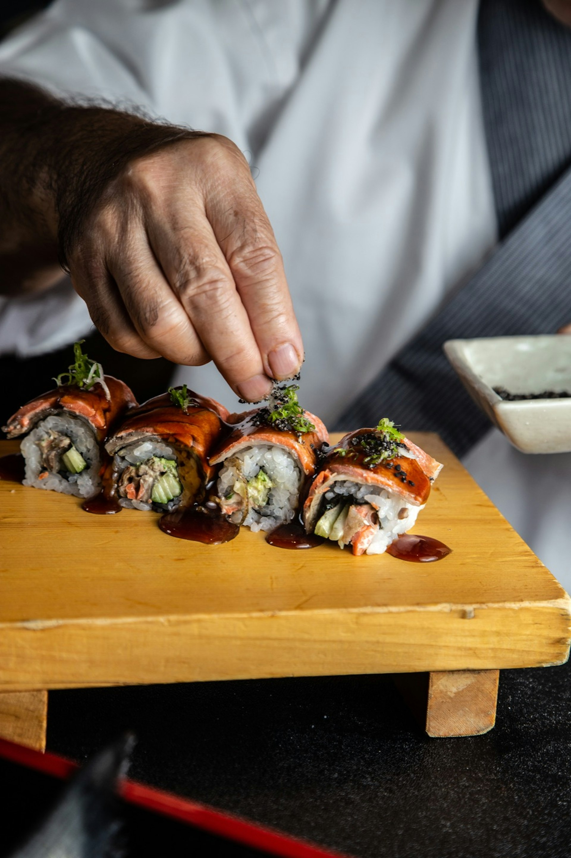 A chef's hand adding ingredients to a BC roll on a wooden cutting board; California roll 