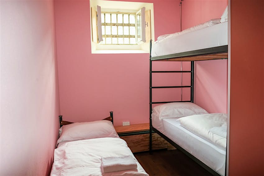 Three dorm beds in a pink hostel room that was once a prison.