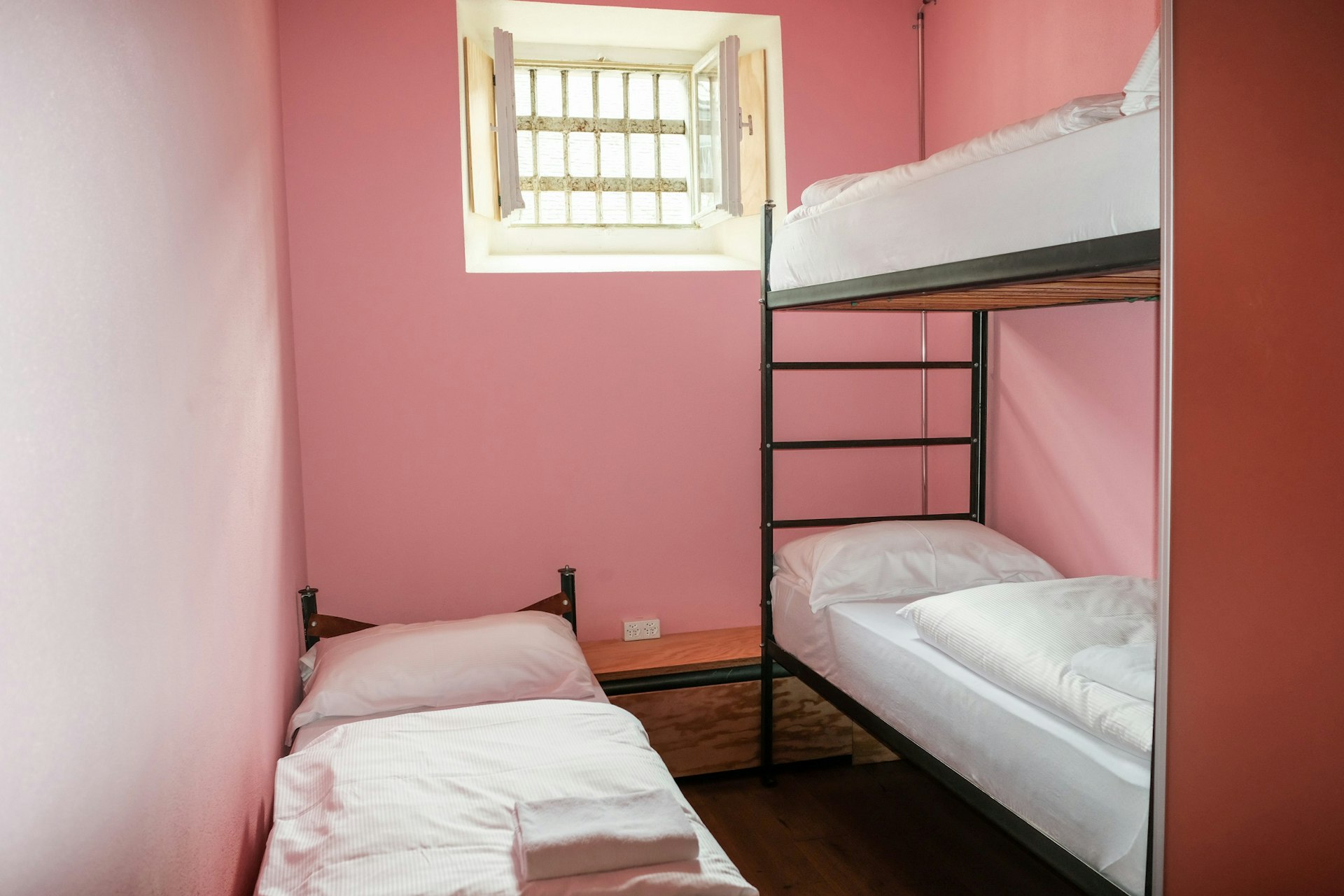 Three dorm beds inside a pink hostel room that was once a prison.