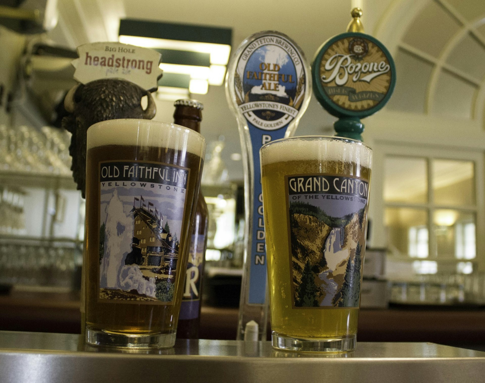 A selection of pint glasses with images from Yellowstone National Park are filled with beer at a bar