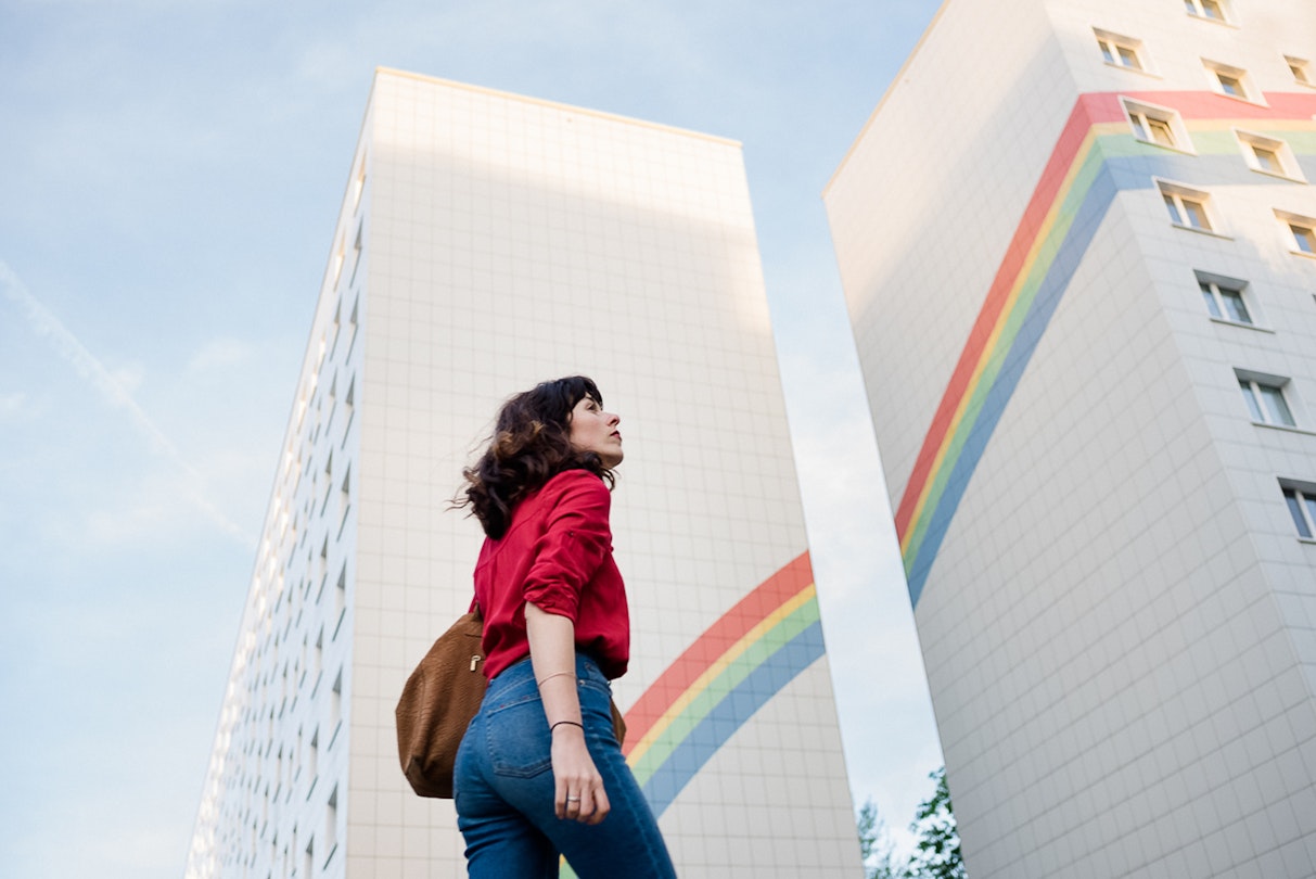 A woman looks to the sky against the the backdrop of a rainbow painted building in Berlin