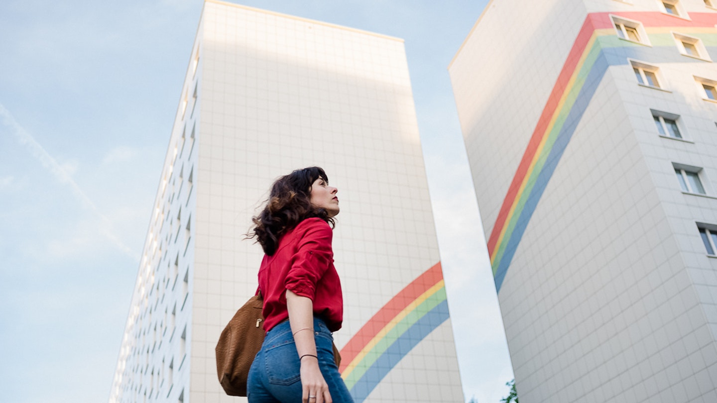 A woman looks to the sky against the the backdrop of a rainbow painted building in Berlin