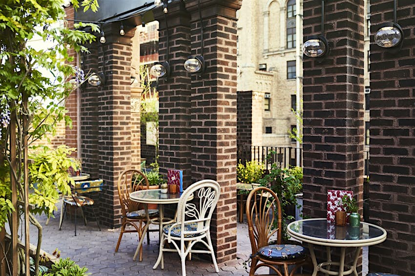 Tables and chairs next to brick cloumns, with potted plands interspersed throughout the rooftop bar in New York City