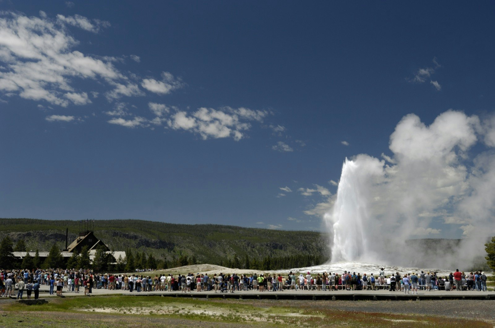 Crowds of people surround the Old Faithful geyser on a summer day during tourist season at Yellowstone National Park