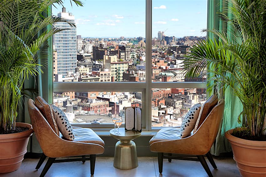 Two chairs next to a window, framed by plants and green curtains; best rooftop pools in New York City