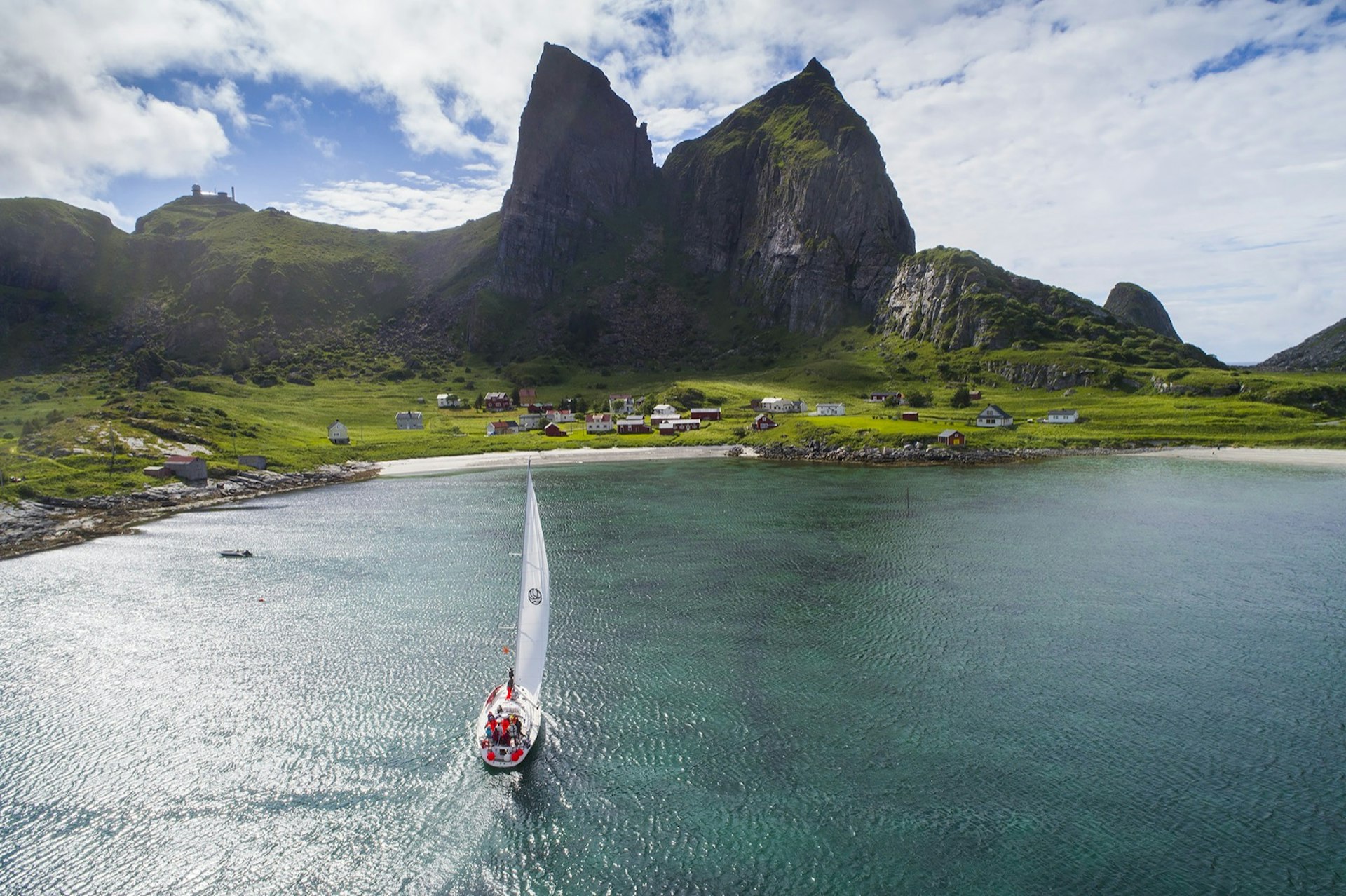 A sail boat heads towards a green shore line with two giant rock mountains in the background