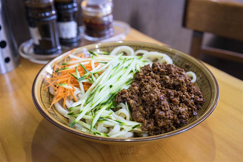 Features - eat-curiously-lead A close up shot of a bowl of zha jiang mian, served at EJ Fine Food restaurant in Melbourne. The dish has fresh shredded vegetables, beef and noodles.