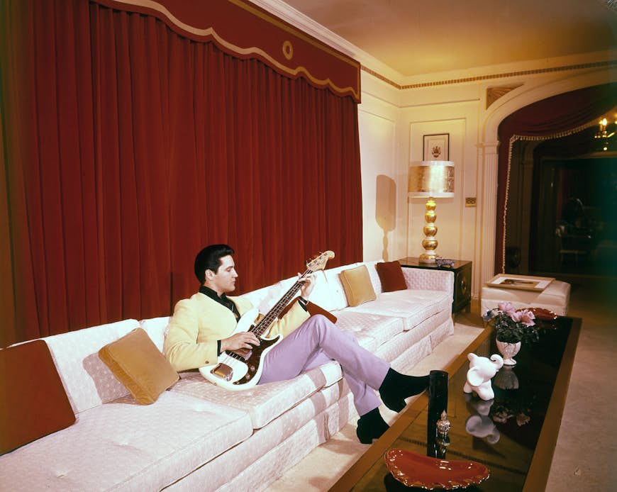 Elvis sitting on a white couch with a bass guitar at Graceland