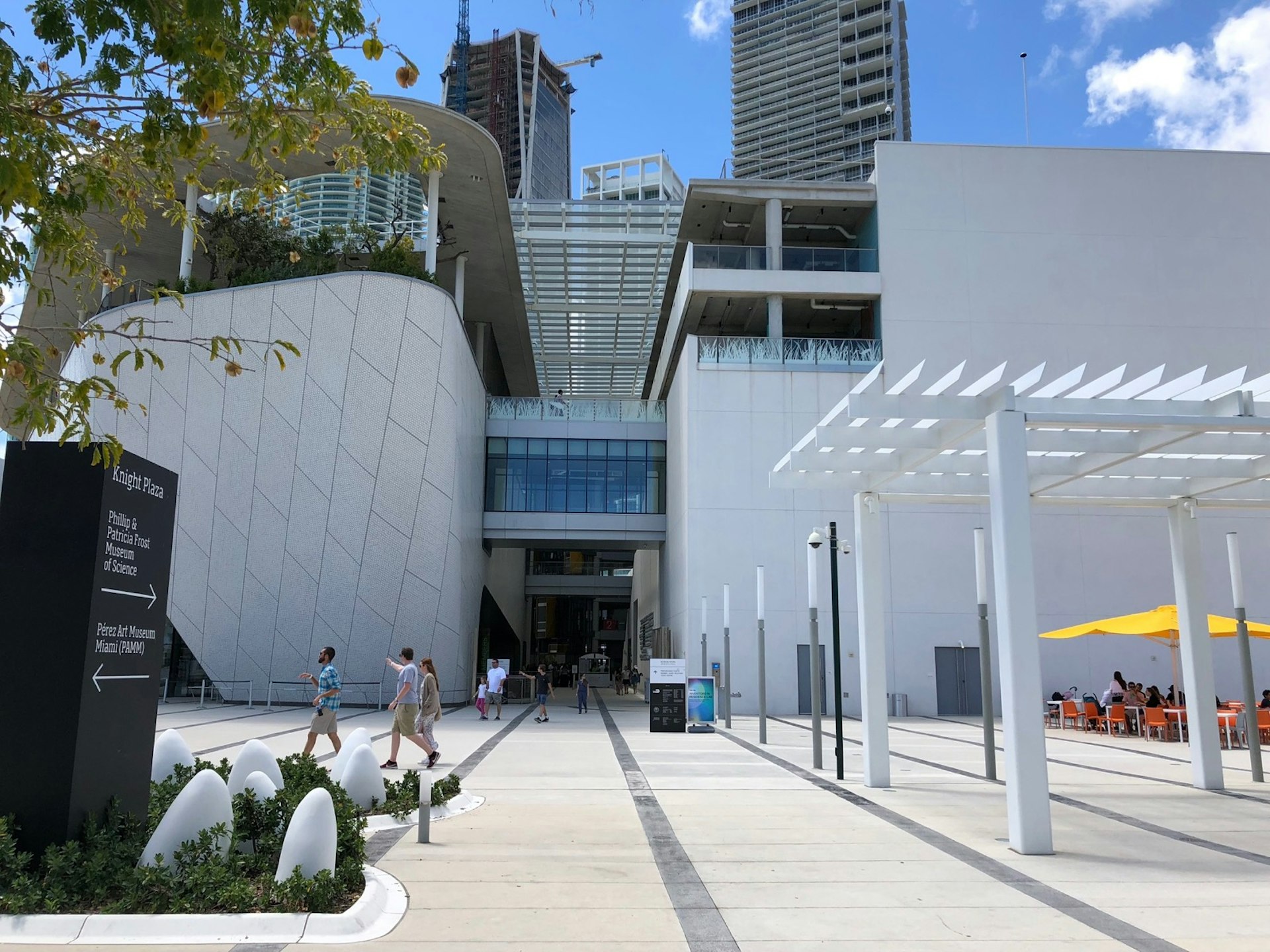 People walk in front of a stark white multi-story art-deco building with a white pergola and glass entrance. Weekend in Miami