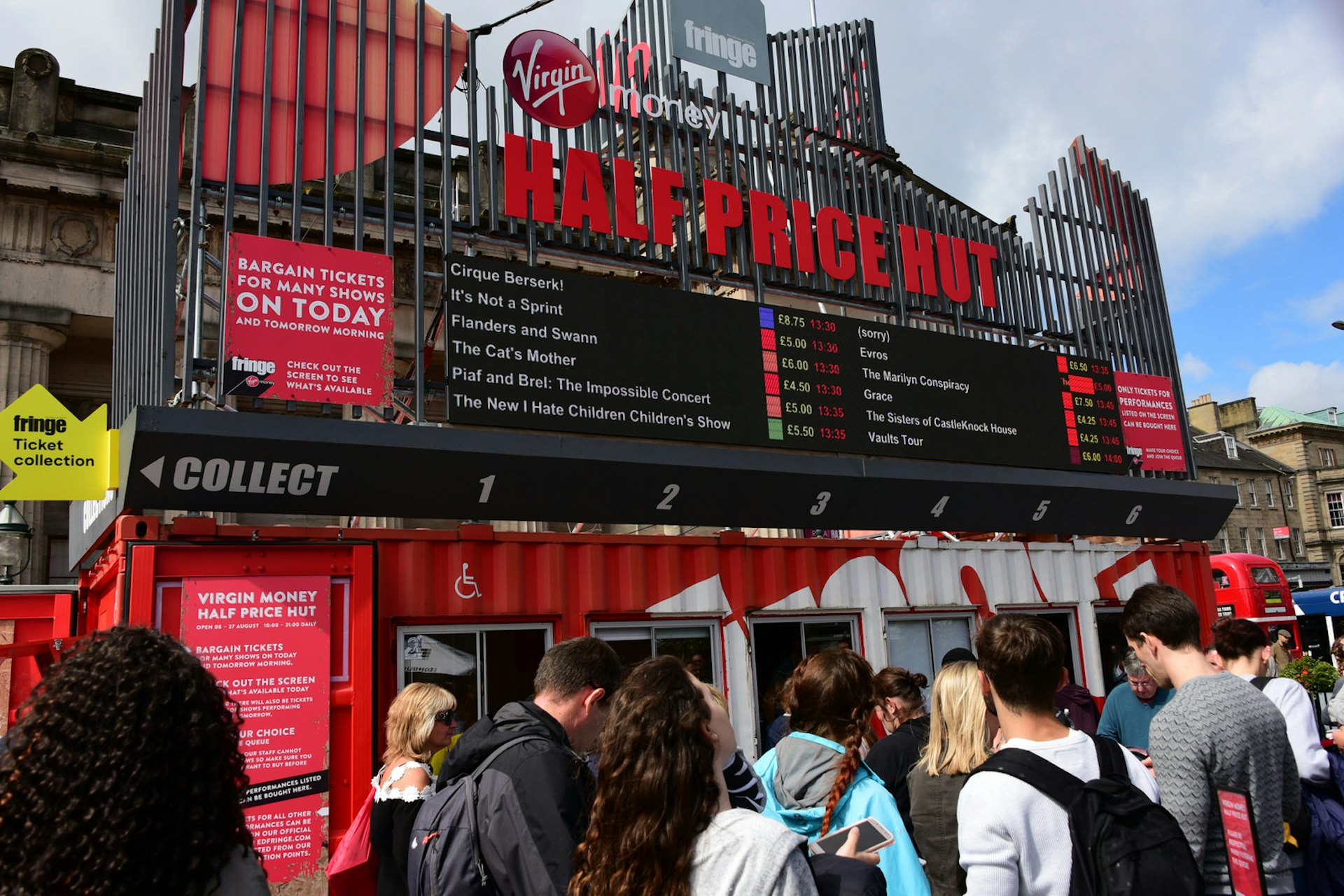 Festival-goers on The Mound precinct queue outside the "Half Price Hut" ticket office during the Edinburgh Festival Fringe. The office is in a shipping container painted red and white with windows to serve customers through. 