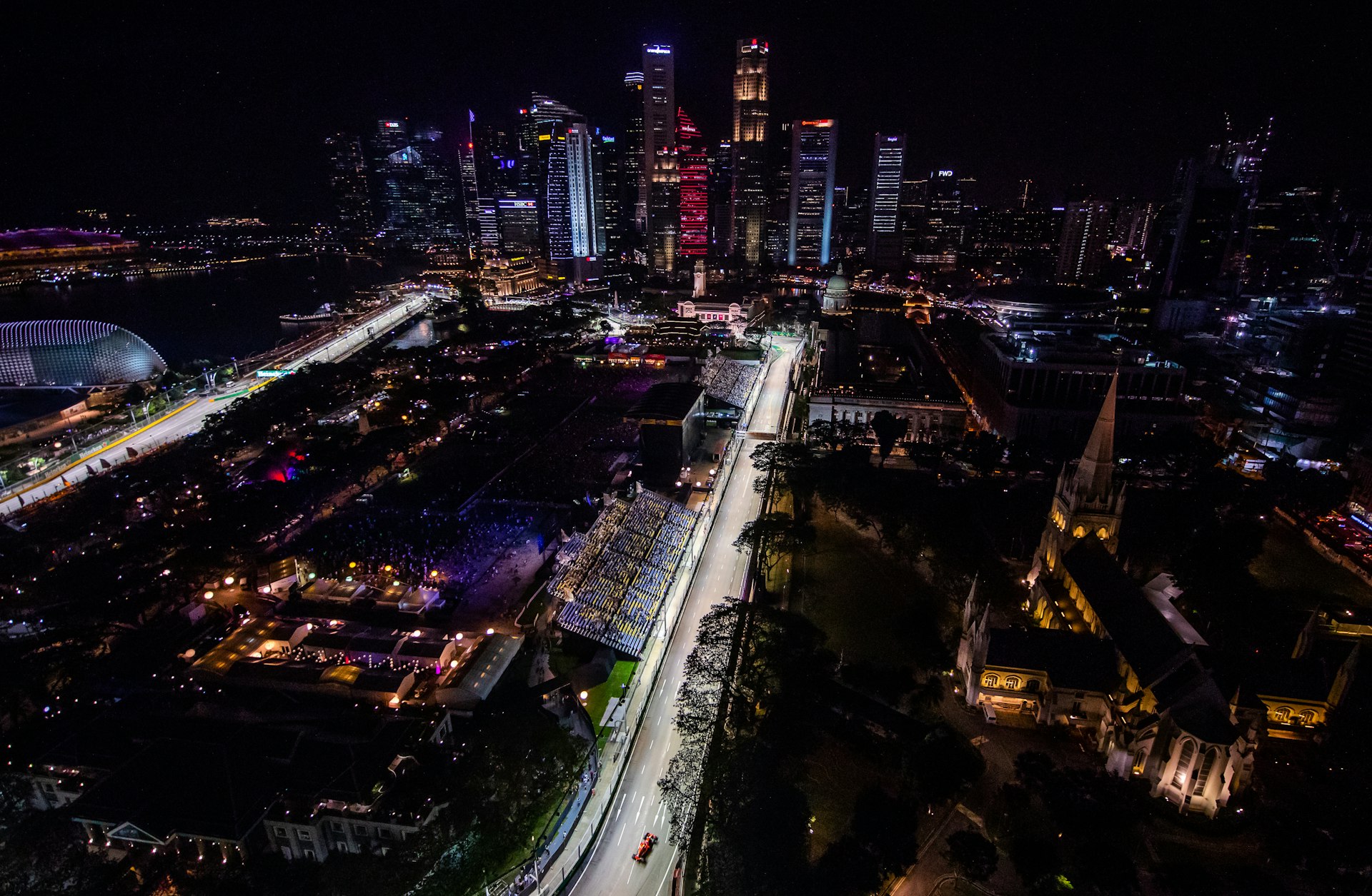 Overhead view at night of the Singapore skyline and racetrack. The track is illuminated and a Ferrari is visible in the foreground.