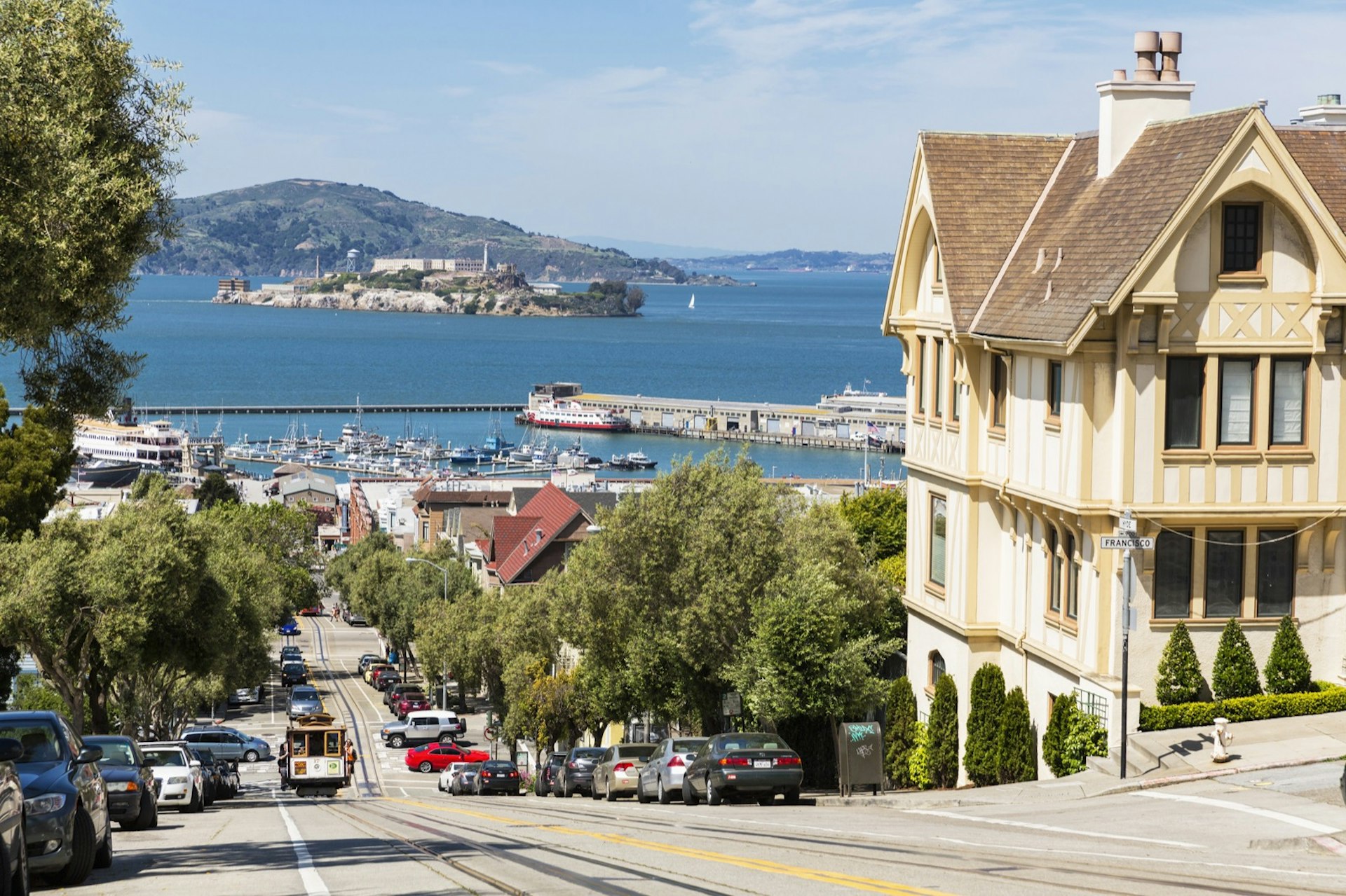 Steep road down with a cable car, ocean in the background and large yellow victorian house in the foreground. Weekend in San Francisco