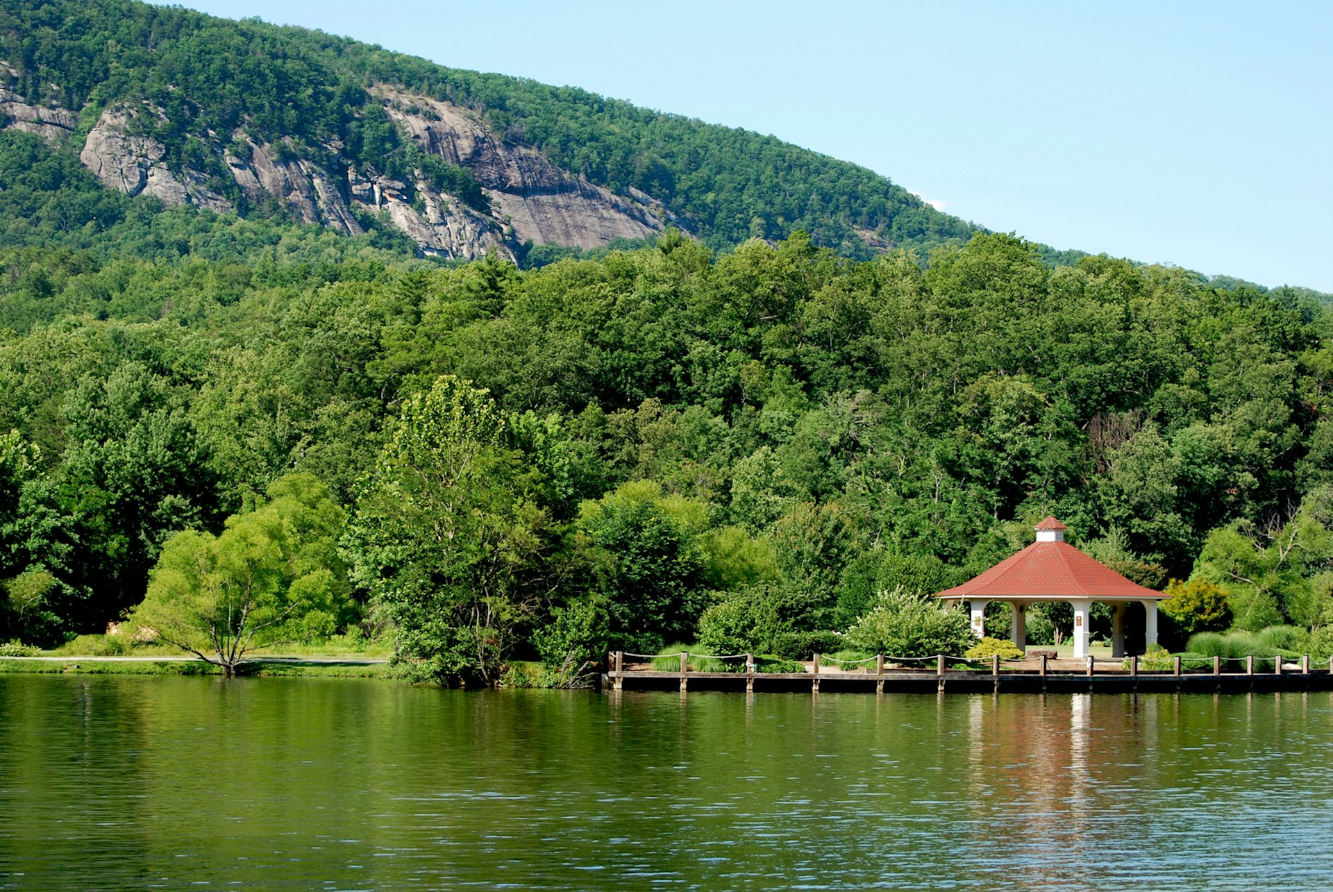 A lake and a small roofed structure, with green trees and a mountain in the background; summer trips in the Southern US