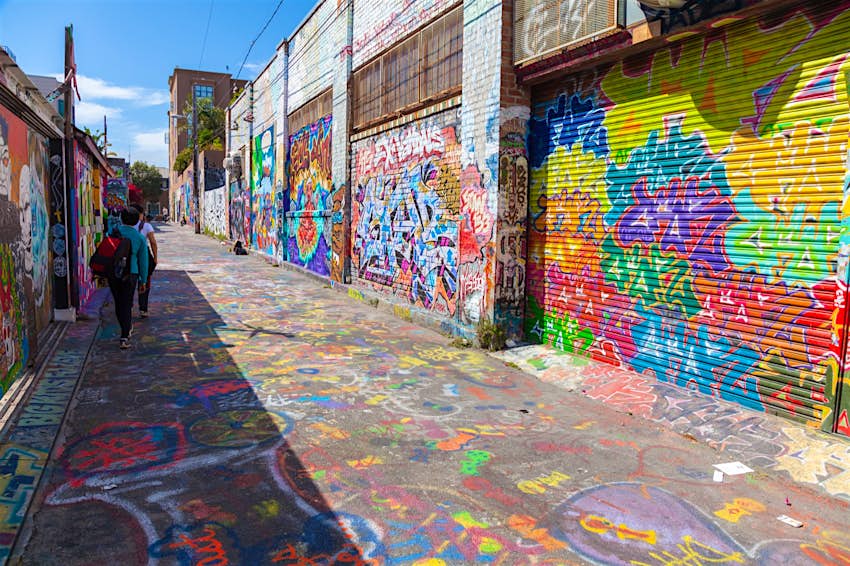 people walk down an alley where the garages are all painted with colorful images. Weekend in San Francisco