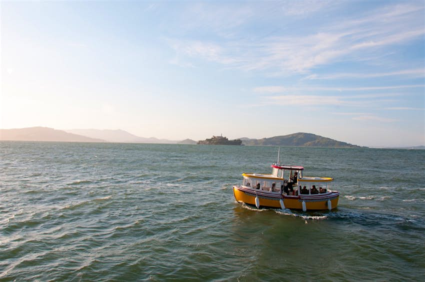 A boat cruises through the ocean towards a setting sun with hilly islands in the background. Weekend in San Francisco