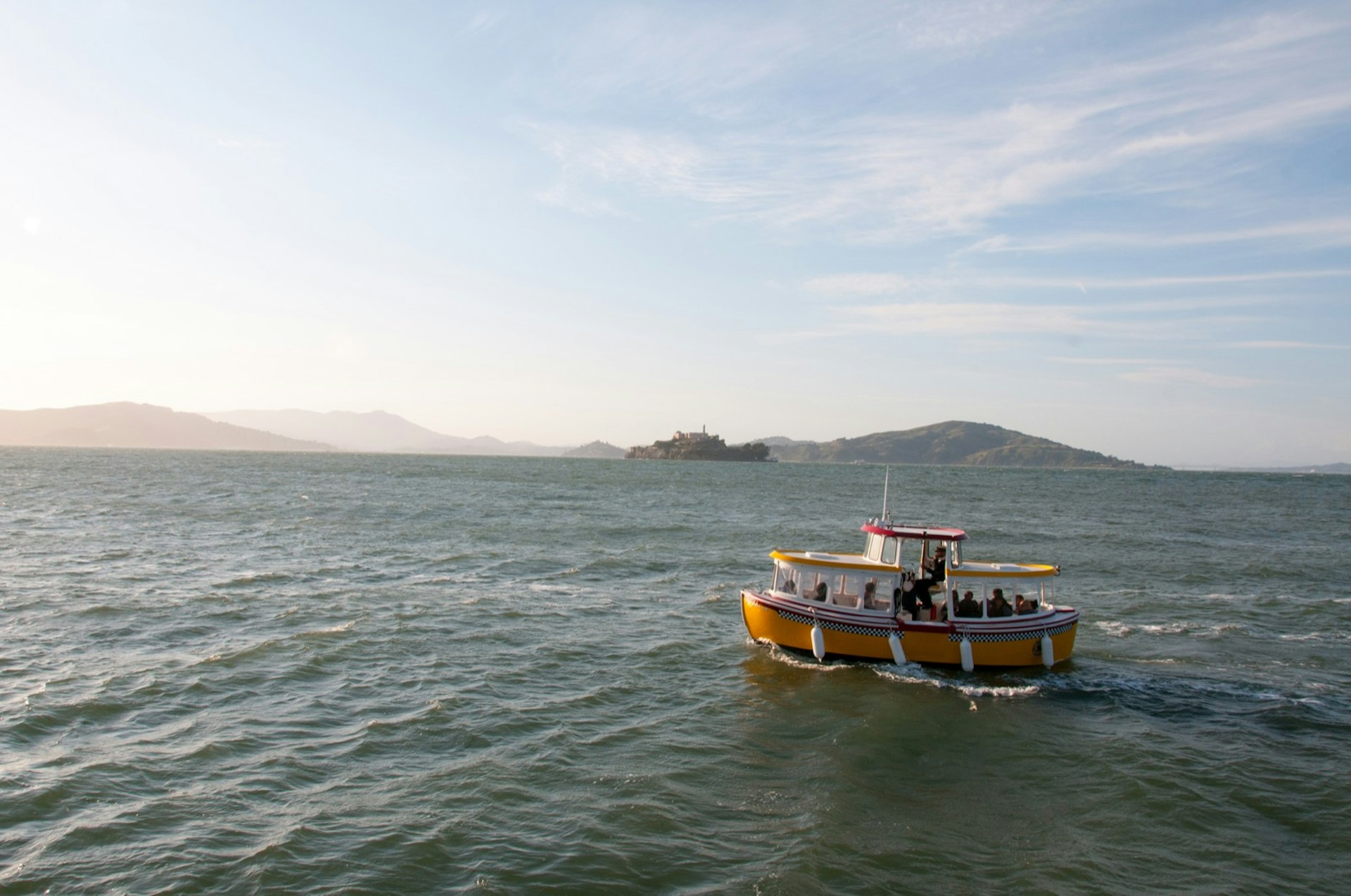 A boat cruises through the ocean towards a setting sun with hilly islands in the background. Weekend in San Francisco