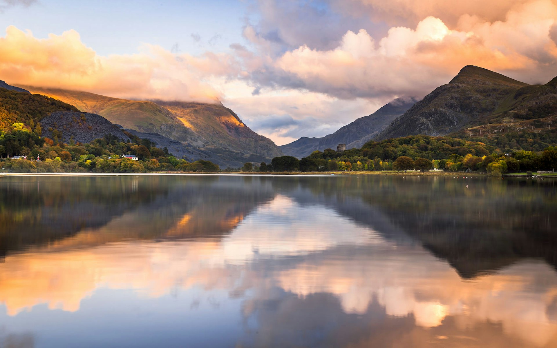 A sunset behind Snowdonia that is reflected in the still water of lake in the foreground.