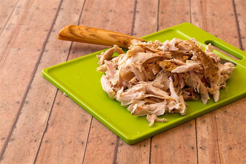 Shredded rotisserie chicken on a green plastic cutting board and carving knife against wood plank background; easy hostel meals