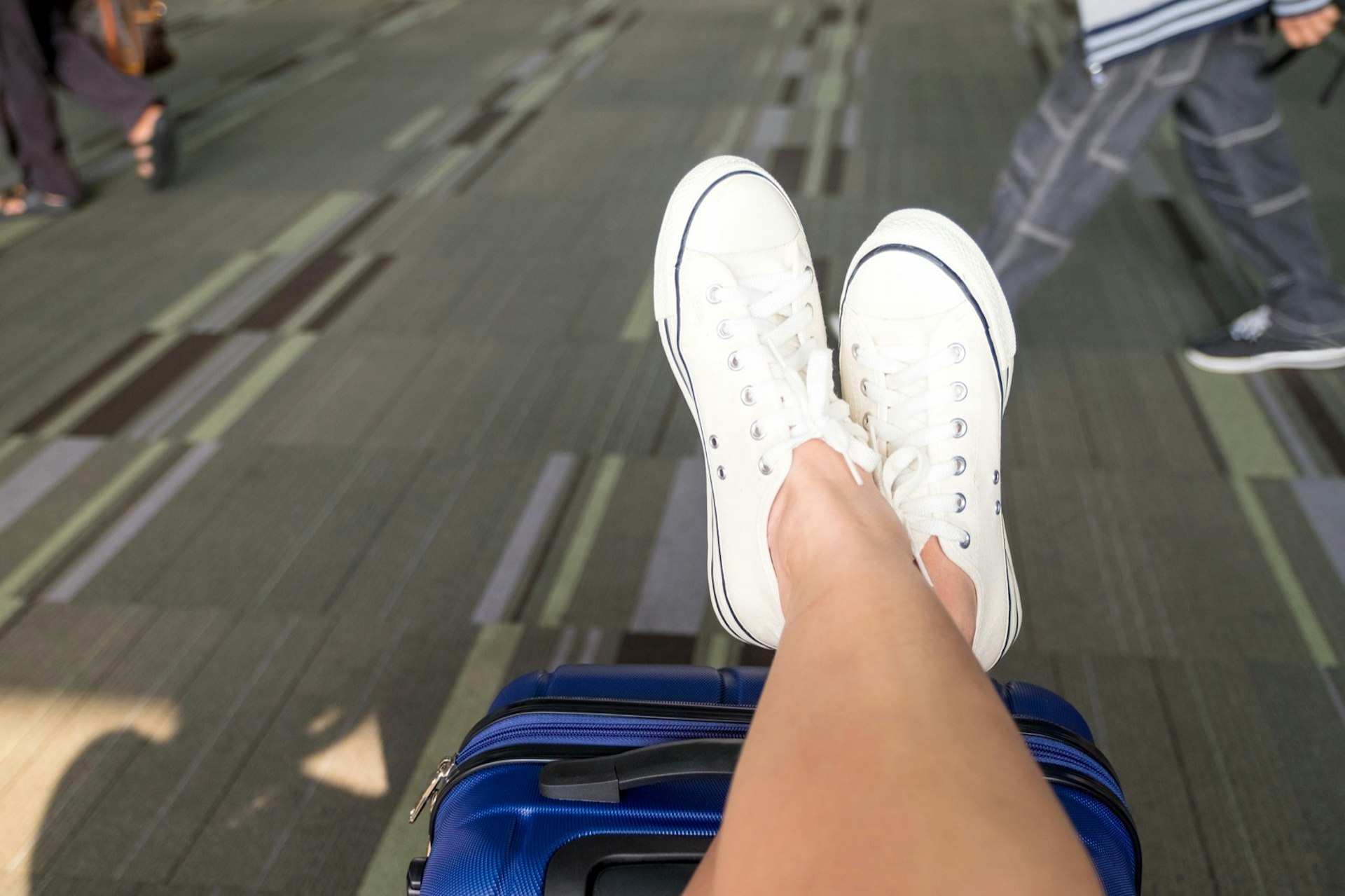 Close up of a person crossing their legs wearing white sneakers propped up on suitcase at an airport terminal; tips for a long-haul flight 