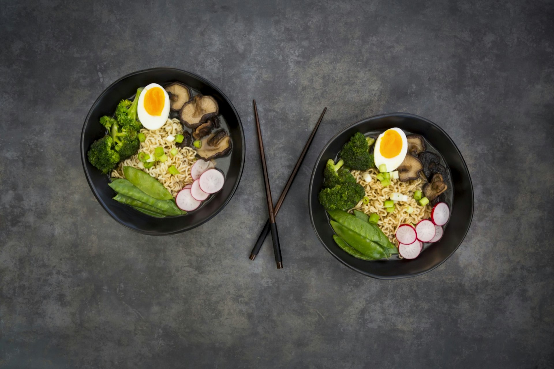 Overhead view of two bowls of ramen with veggies and boiled eggs, with chopsticks in the middle; easy hostel meals