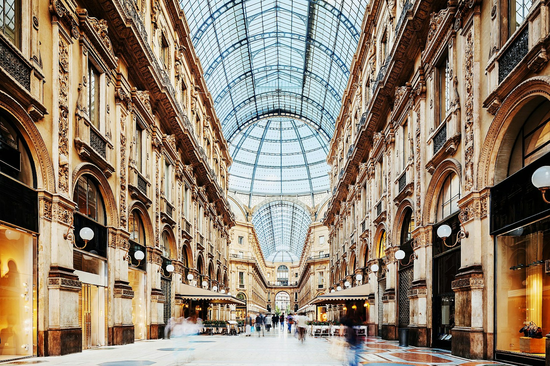 Inside the neoclassical Galleria Vittorio Emanuele II shopping arcade, looking up to its roof made of iron and glass, with upmarket stores either side of the arcade.