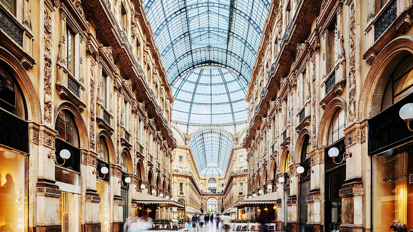 Inside the neoclassical Galleria Vittorio Emanuele II shopping arcade, looking up to its roof made of iron and glass, with upmarket stores either side of the arcade.