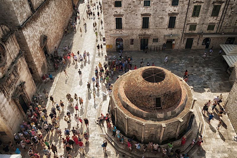 A high-angle view of a crowd around the city wall and Onofrio's Fountain in Dubrovnik.
