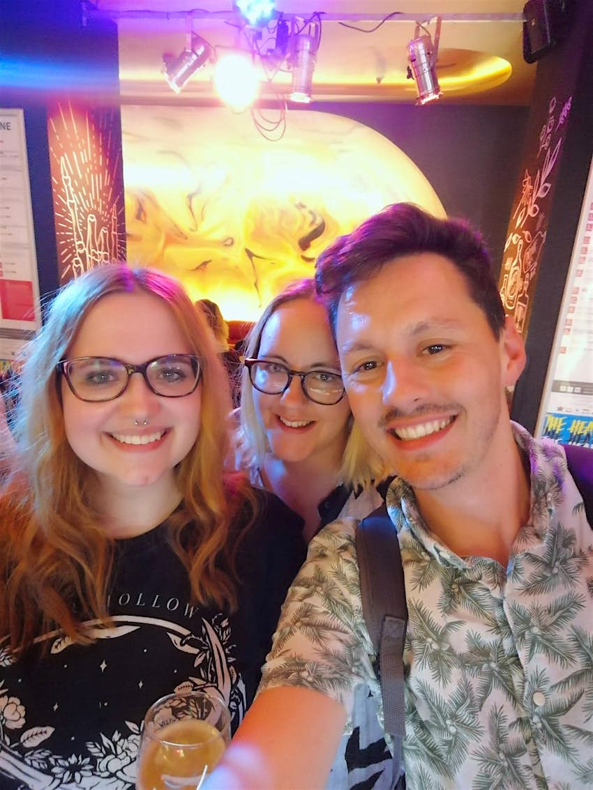 Two young women and a guy smile for the camera in a bar.