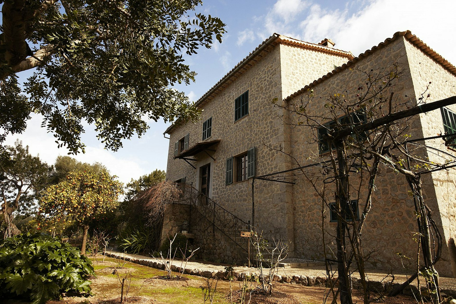 The three-storey stone building housing Casa Robert Graves, set in a garden full of trees.