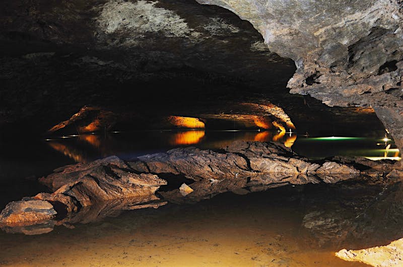 Features - LostSea-baa5e5e06ec8 A large craggy rock sits in a pool of shallow water deep in a dark cave. In the background lights illuminate different paths in the cave