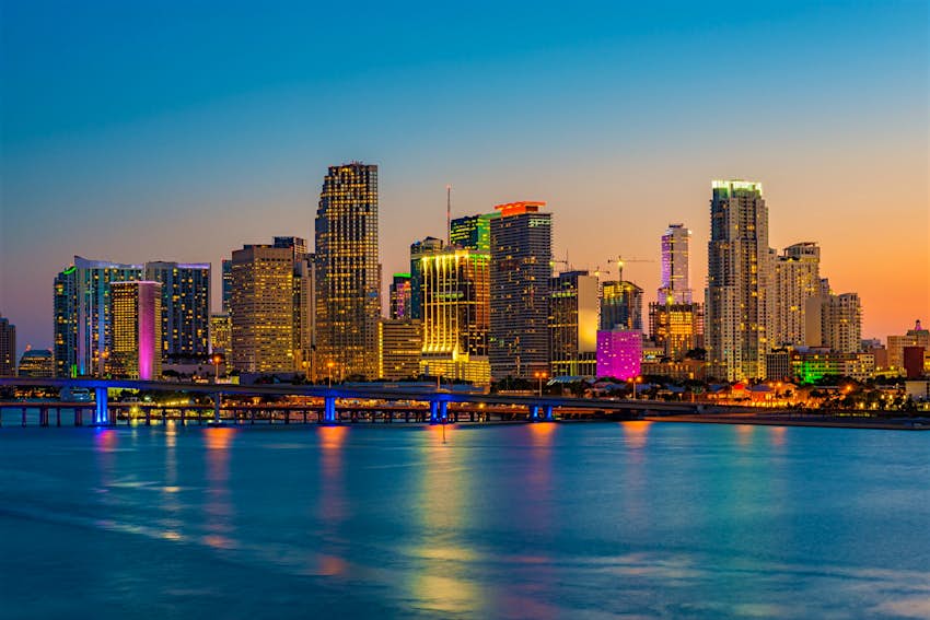 Skyline of Miami around Sunset, with neon pinks and purples reflected in the water of the bay. Weekend in Miami