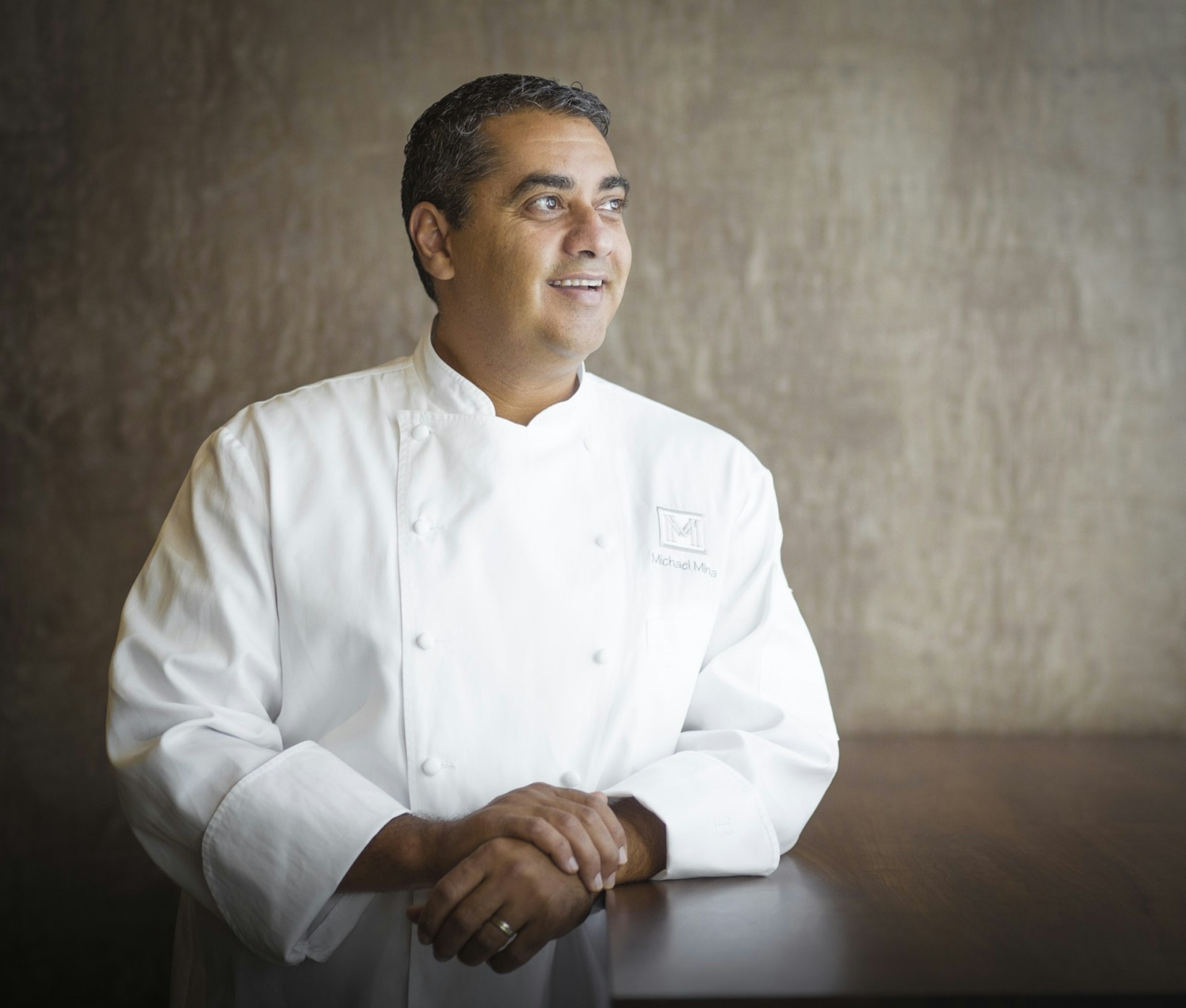 A publicity photo of celebrity chef Michael Mina smiling against a grey-brown backdrop