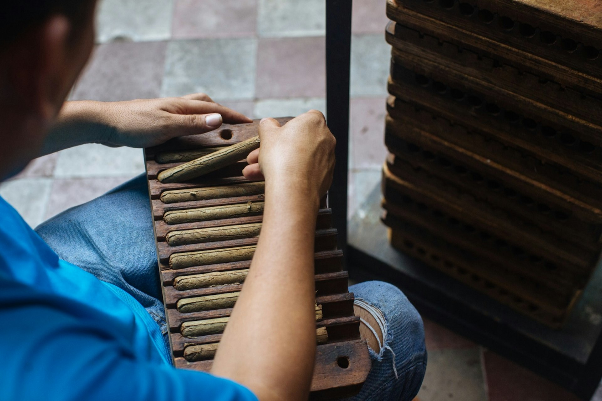 A man places a finished rolled cigar on the top row of a cigar holder. There's a collection of cigar holders on a cart; Nicaragua travel.