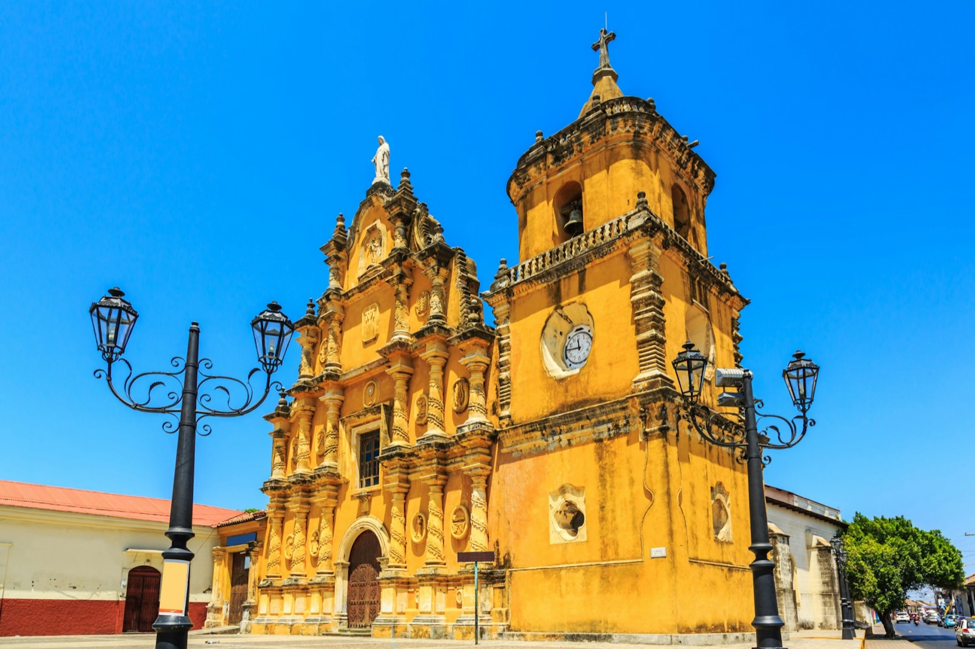 A baroque-style bright yellow church on a corner in the city of León. In front there are a pair of gothic-styled light posts; Nicaragua travel. 
