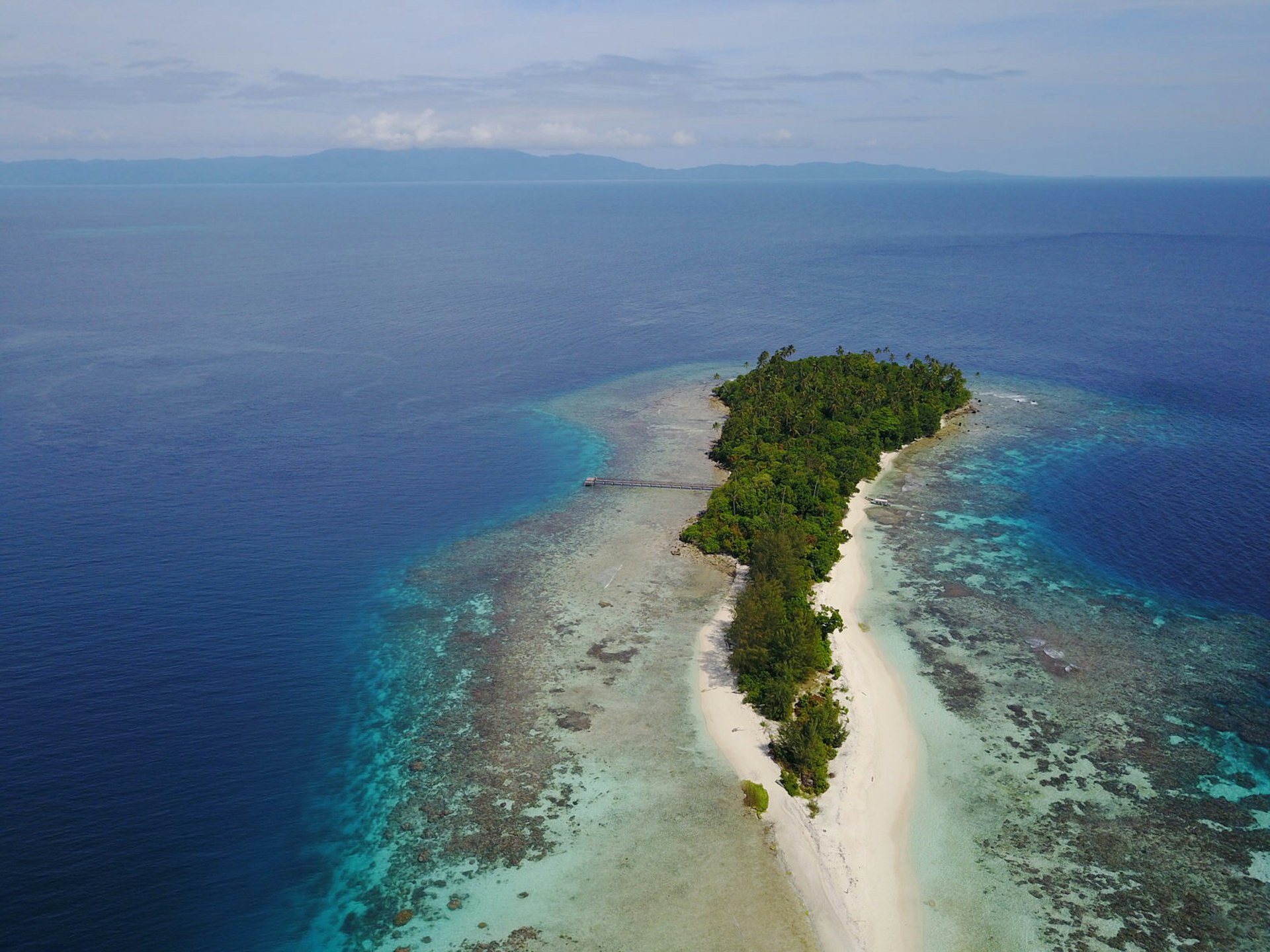 An aerial shot of Njari Island. A thin island with white sand beaches and dense forest inland surrounded by the bright blue Pacific Ocean