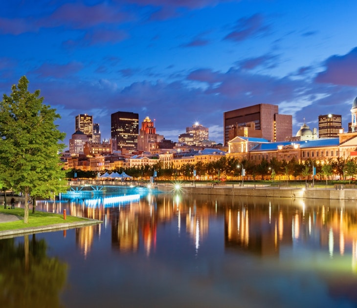 blue and purple clouds cross the sky at twilight as a beautiful skyline of lighted historic buildings is reflected in the waterfront of the Old Port of Montreal