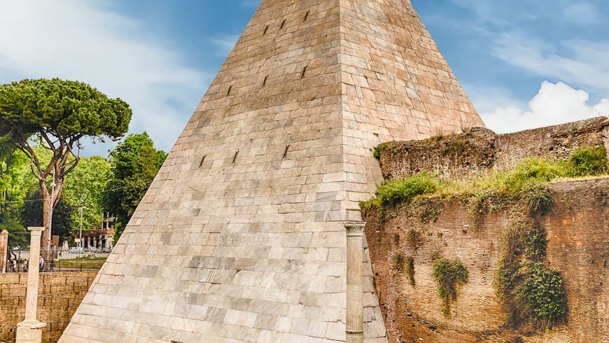 A crisp-edged steep-sided stone pyramid rises from a lawn; large stone walls branch out from either side