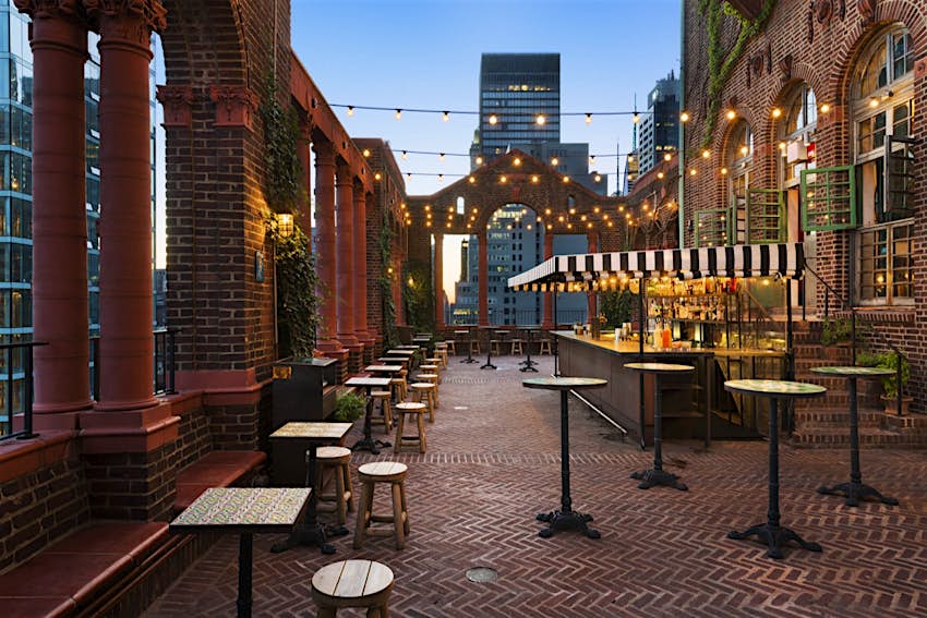 Tables and stools lined up around a rooftop bar in New York City, with string lights overhead