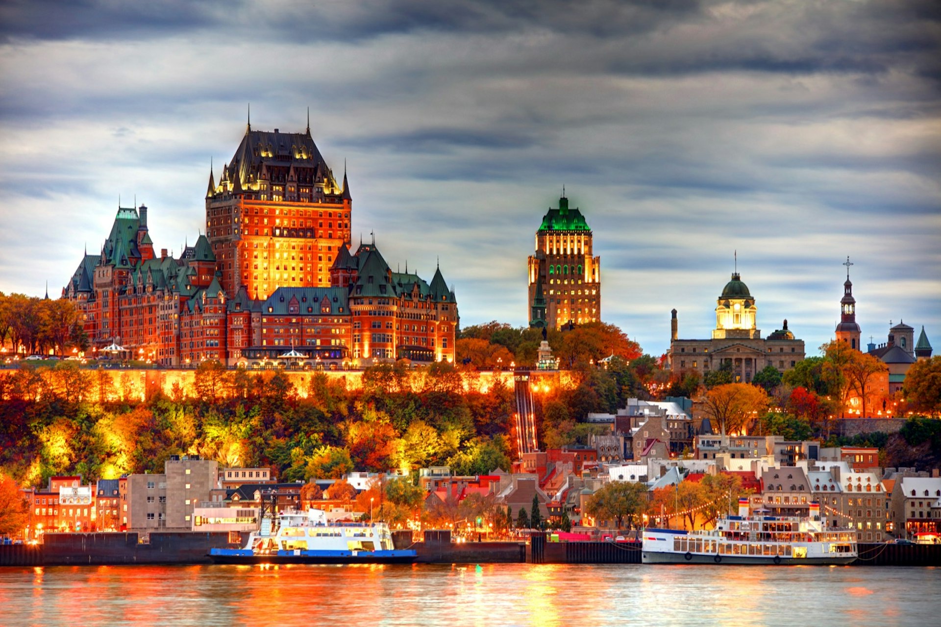 Orange lights reflect the skyline of Quebec City in the river below. Best day trips from Montréal