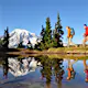 Two hikers walk by a small pond with Mt. Rainier behind. Day trips from Seattle