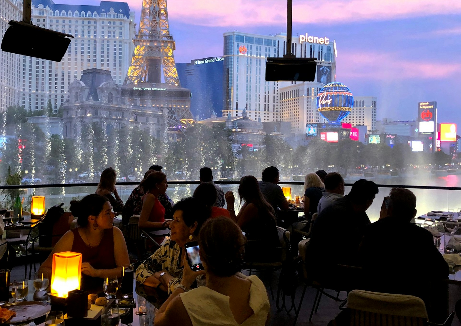 Diners sit in the dark at sunset as a fountain show goes on right outside the confines of their patio table. Celebrity chef restaurants in Las Vegas