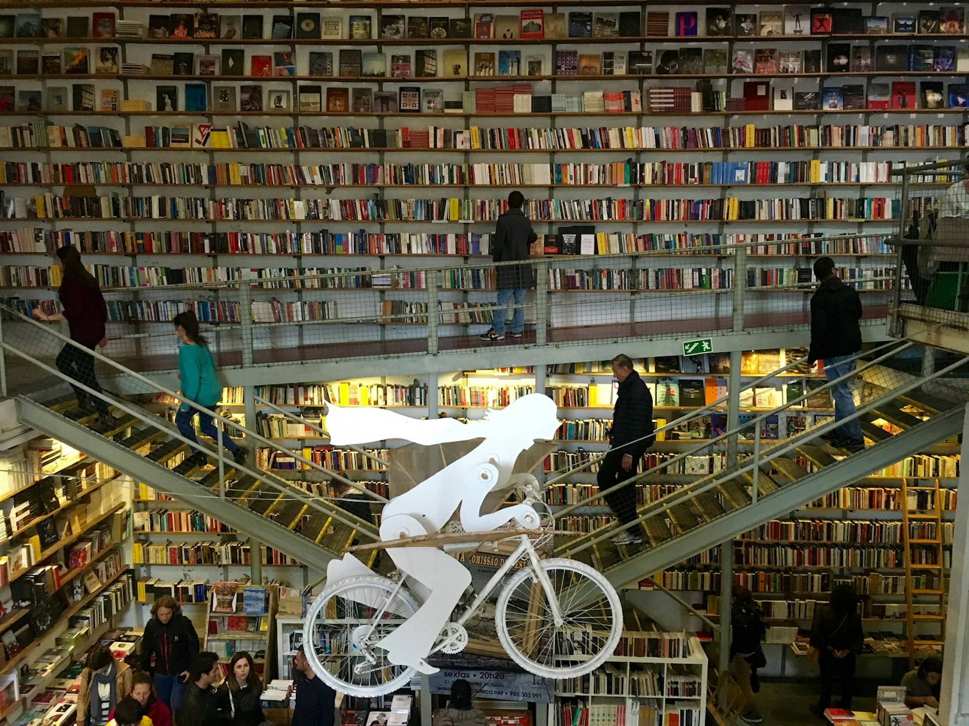 An artwork of a figure on a bicycle is in the foreground. Either side, staircases go up to walkways where the walls are lined with books