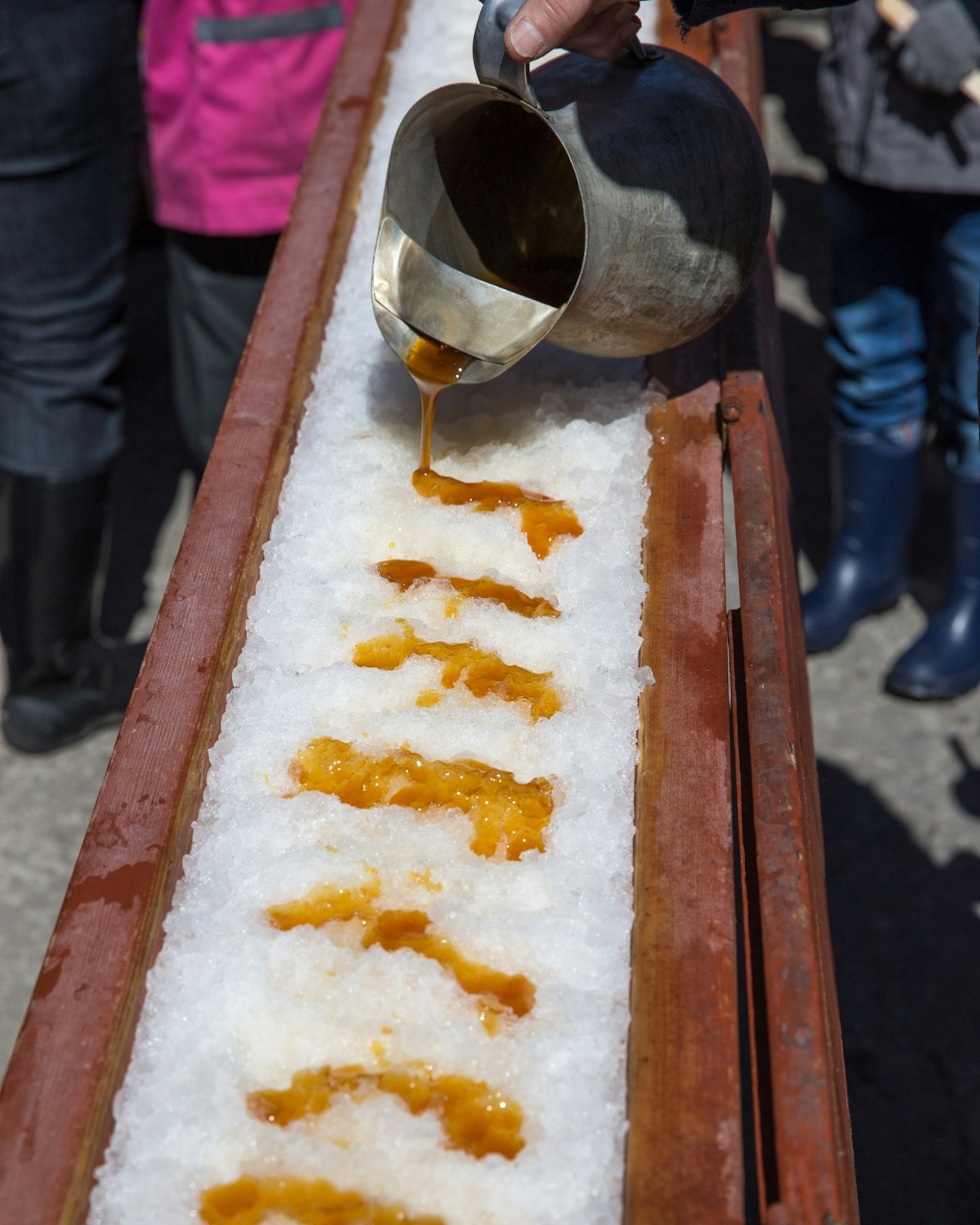 Hot Maple sugar on snow at a sugar shack. A jar of maple sugar is pouring the golden liquid on freshly compacted snow. Best day trips from Montréal