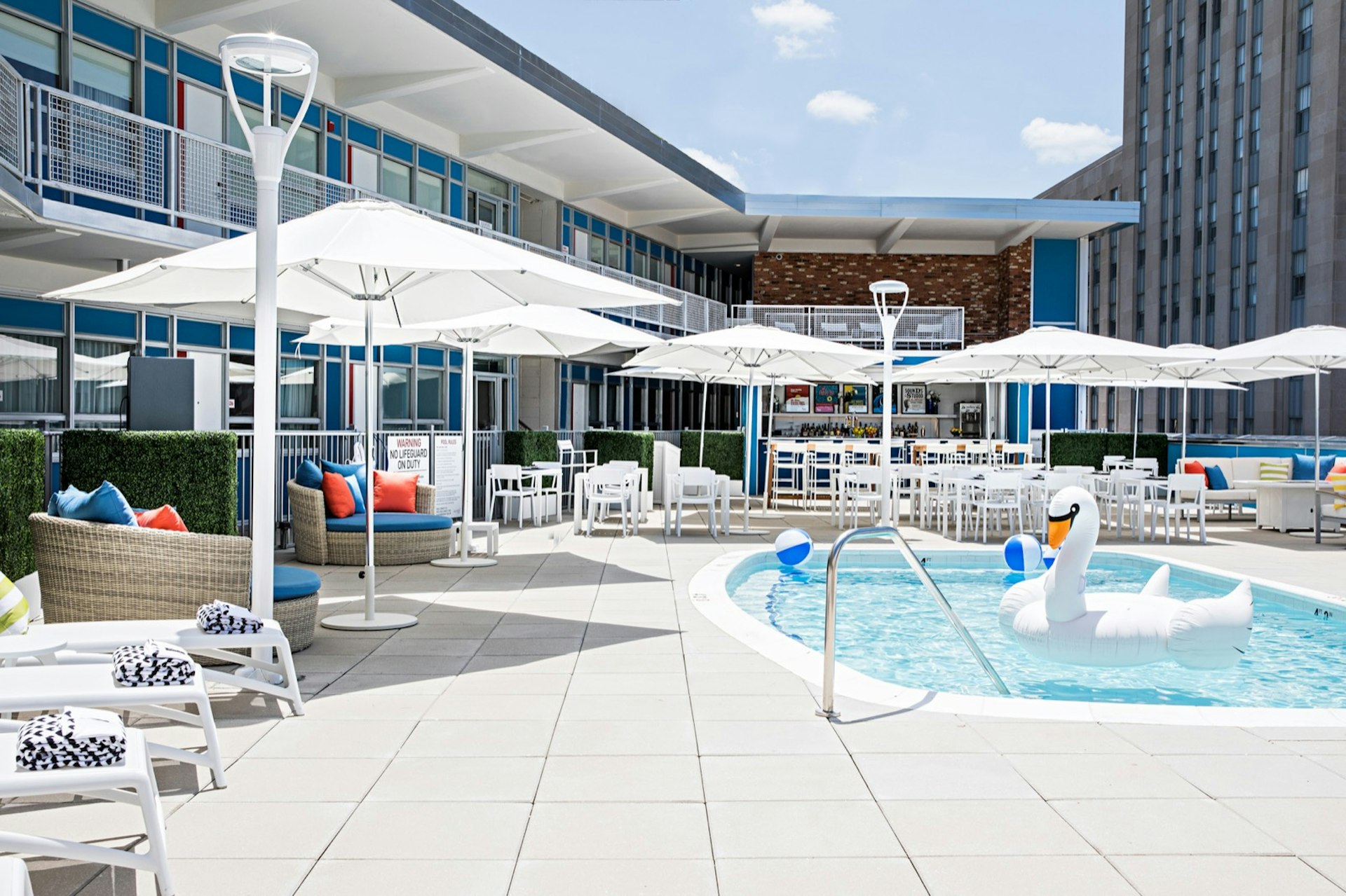 The pool area of Unscripted hotel, with a large inflatable swan and beach balls in the water and umbrellas surrounding